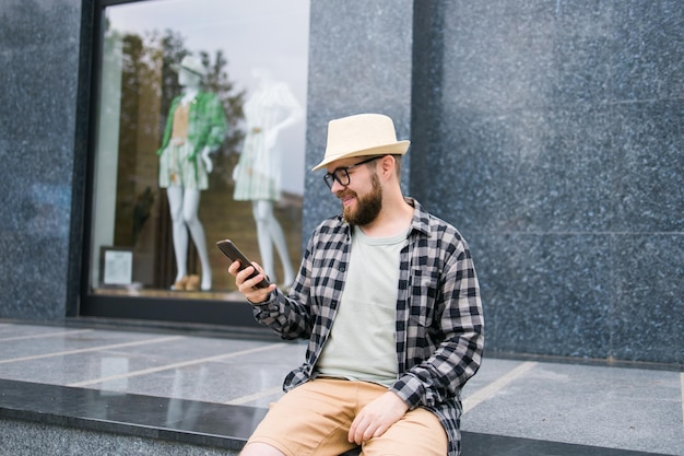 Un turista masculino sonriente usa un teléfono inteligente durante las vacaciones de verano, las tecnologías y la aplicación de las redes sociales
