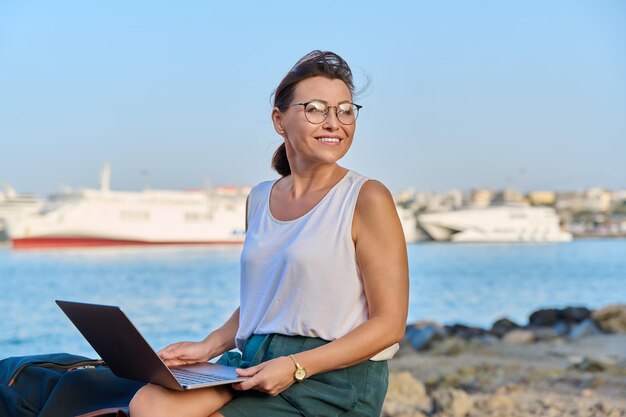 Turista de mediana edad con una mochila en el puerto usando una computadora portátil