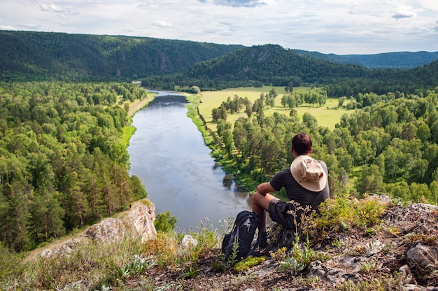 Un turista con una mochila y una cámara en una roca disfrutando de una vista del valle del río