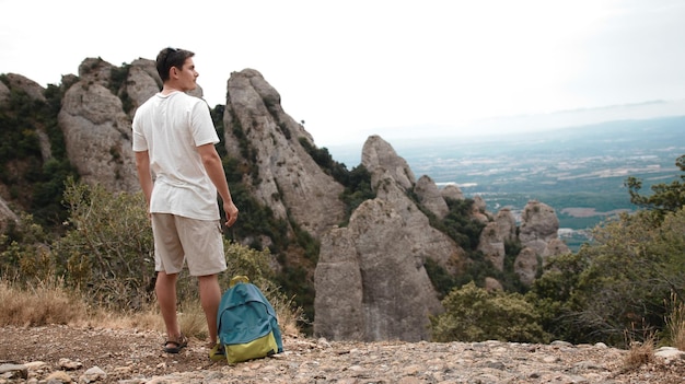 Foto un turista con una mochila se para en la cima de una montaña y mira el paisaje montañoso.