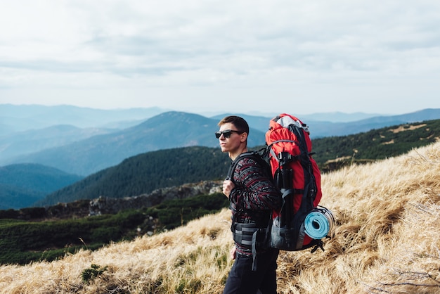 Turista con una mochila enorme en la cima de una cordillera.