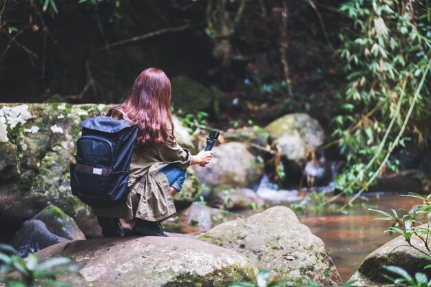 Una turista con mochila graba un video de la cascada en el bosque con una cámara de acción.