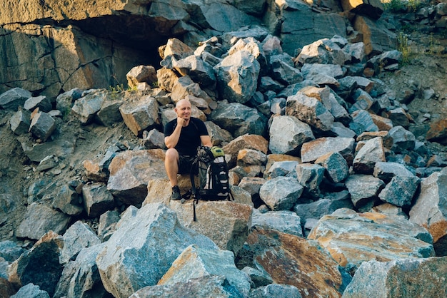 Un turista con una mochila en la mano se sienta sobre una piedra en el fondo de las rocas en el día Un viajero mira la localidad que tiene delante