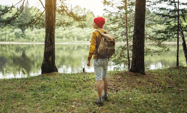 Un turista con una mochila y un sombrero rojo camina en el bosque entre los árboles.