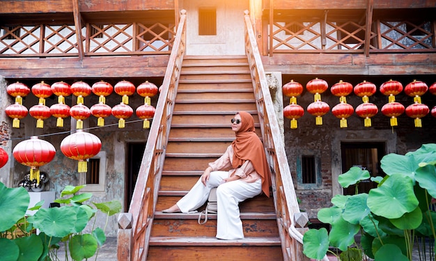 Turista muçulmano feliz da mulher que senta-se em uma escadaria em uma atmosfera chinesa da casa, mulher asiática no feriado. Conceito de viagens. Tema chinês.