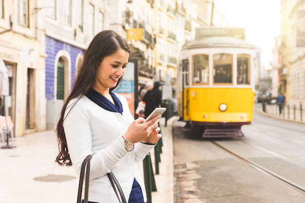 Turista de la mujer en Lisboa que comprueba el horario del tranvía en su smartphone