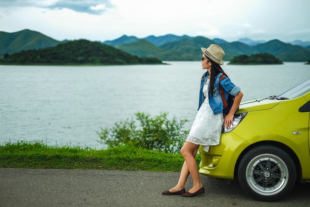 Turista de mujer de pie cerca del coche y feliz por la vista de la montaña y el lago