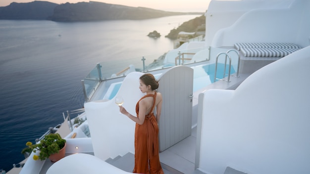 Turista de mujer en vestido precioso con copa de vino relajante al atardecer