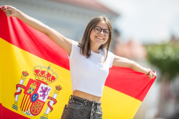 Turista de niña feliz caminando en la calle con bandera española.