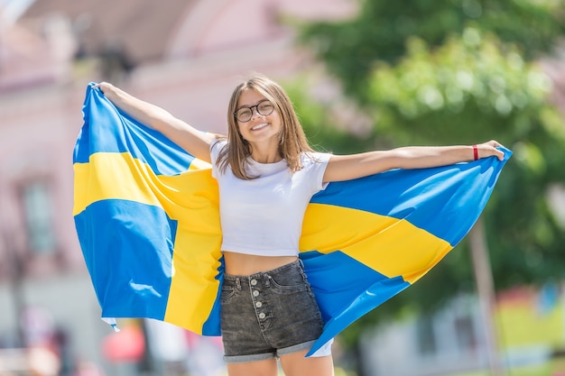 Turista de niña feliz caminando en la calle con la bandera de Suecia.