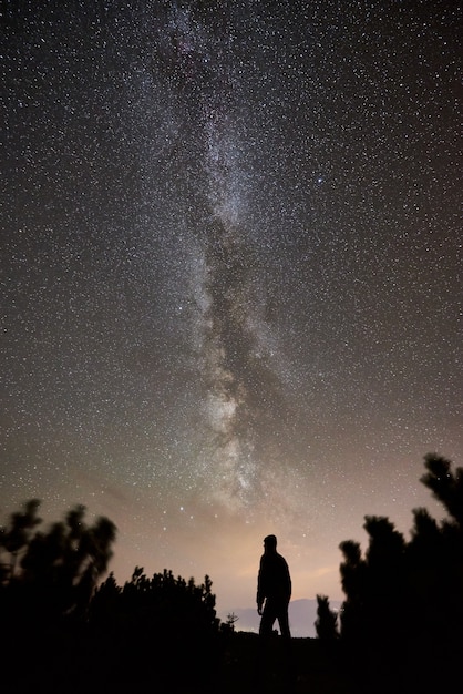 Turista en la noche acampando en la cima de la montaña bajo el cielo estrellado