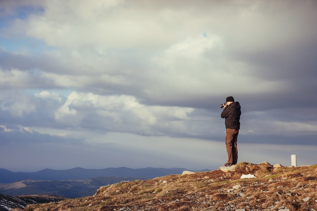 Turista olha a paisagem. Fotógrafo no topo da montanha