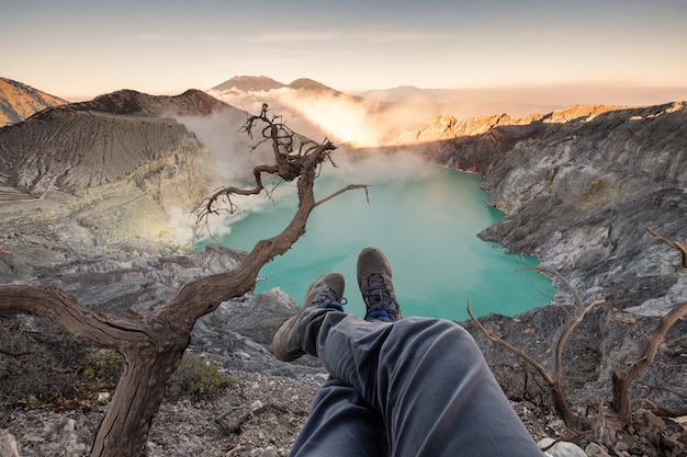 Turista pendurado as pernas na cratera kawah ijen com lago esmeralda ao nascer do sol. java oriental, indonésia