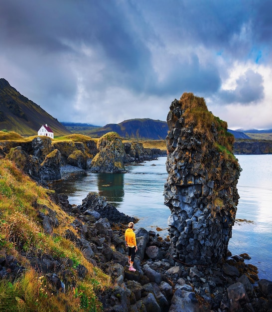 Turista en una playa rocosa mira una pequeña casa en Arnarstapi Islandia