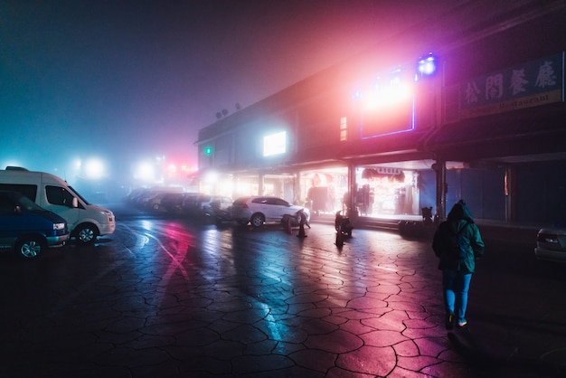 Turista que anda na rua na noite com névoa e luzes coloridas da construção no inverno em Alishan, Taiwan.