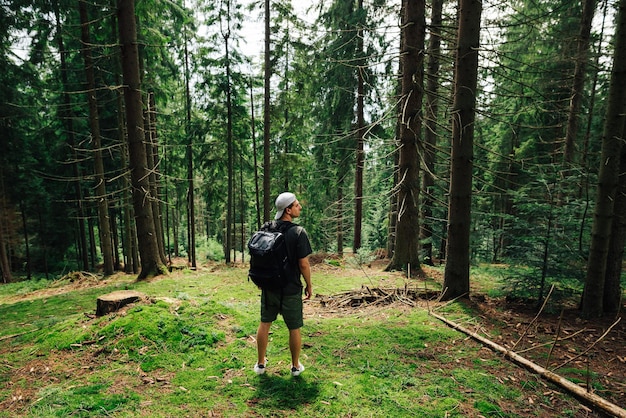 turista con ropa informal se para en el musgo en el bosque en una subida a la montaña con una mochila