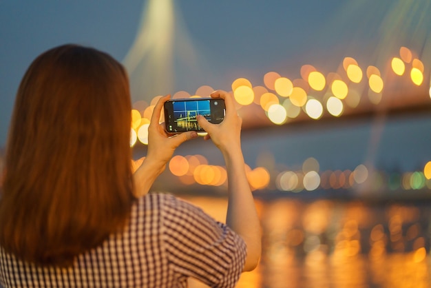 Turista sin rostro con cabello largo tomando foto vista urbana en el móvil