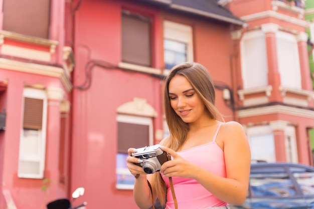 Turista rubia en una calle con casas con fachadas coloridas tomando una foto con la cámara vintage