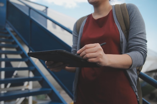 Una turista rubia chequeando la notificación entrante en su teléfono inteligente sentada en el asiento del avión con un netbook Una joven mujer de negocios comparte medios desde el teléfono a la computadora portátil durante el vuelo en avión