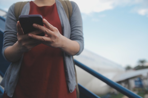 Una turista rubia chequeando la notificación entrante en su teléfono inteligente sentada en el asiento del avión con un netbook Una joven mujer de negocios comparte medios desde el teléfono a la computadora portátil durante el vuelo en avión