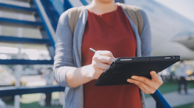 Turista rubia chequeando la notificación entrante en el teléfono inteligente sentada en el asiento del avión con un netbookJoven mujer de negocios comparte medios desde el teléfono en la computadora portátil durante el vuelo en avión