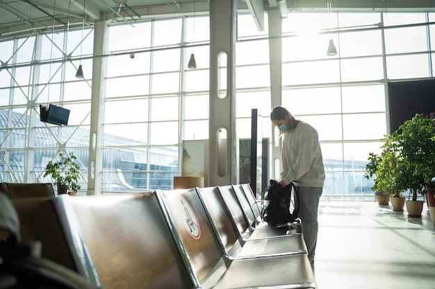 Turista en la sala de espera del aeropuerto buscando algo en su mochila