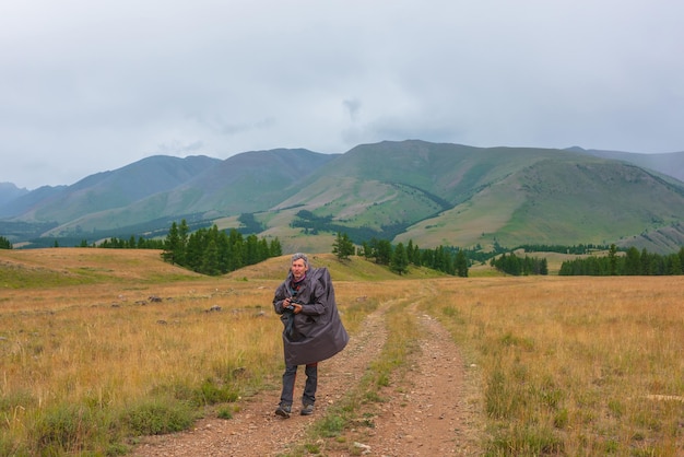 Turista satisfecho regresa de las montañas nublado Hombre feliz en impermeable camina a través de colinas y bosques con mal tiempo El viajero va hacia la aventura Caminante y cordillera bajo un cielo nublado