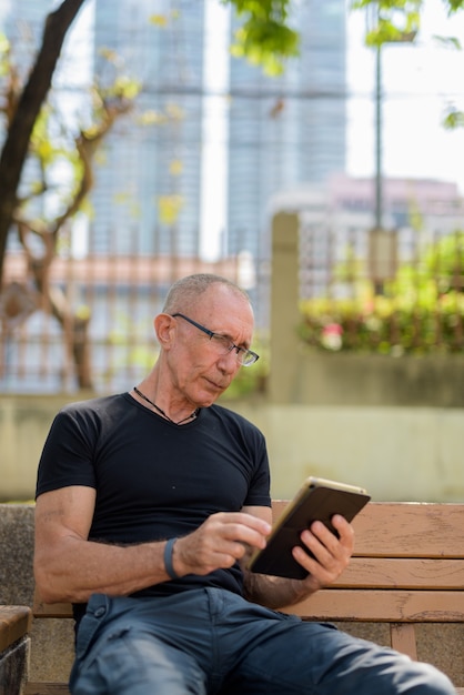 Turista sênior careca usando tablet digital em um banco de madeira