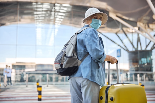 Turista sênior com uma mala de viagem e uma mochila olhando para a frente