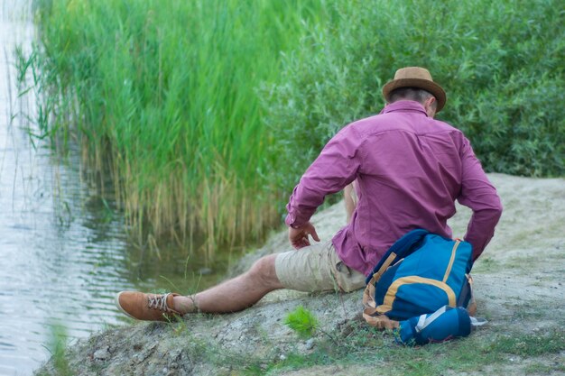 El turista se sienta en la orilla del lago con una mochila para viajar.