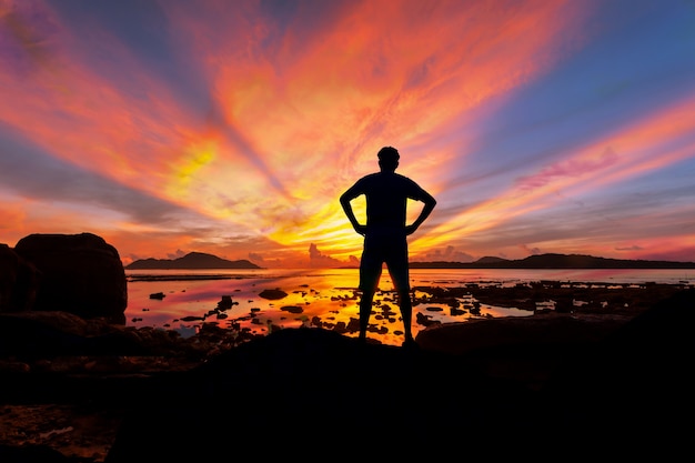 Turista solo del hombre que se coloca en la piedra en el mar tropical y que disfruta de paisaje durante sunris