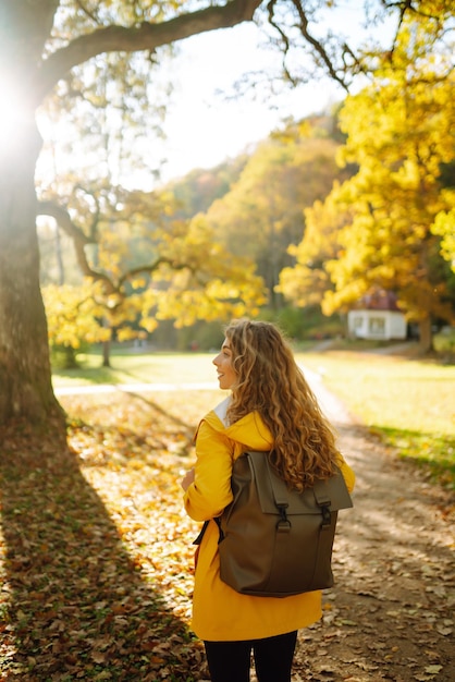 Un turista sonriente con un abrigo brillante camina por un parque de otoño en un clima soleado Concepto de viaje