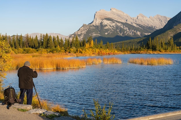 Turista tomando fotografías en Vermilion Lakes a orillas del lago en la temporada de follaje de otoño al atardecer