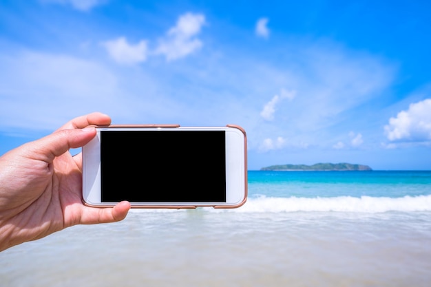 Turista usando el teléfono en la playa con la mano del mar sosteniendo un teléfono inteligente móvil blanco concepto de trabajo de viaje fondo borroso de cerca