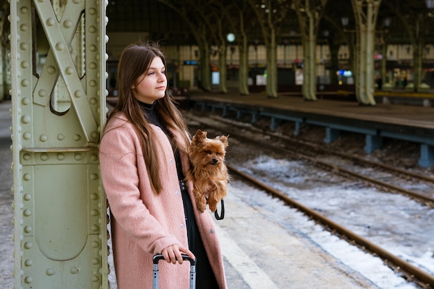 Turista viajante mulher anda com bagagem e cachorro na estação de trem em casaco rosa, o conceito de um ac ...