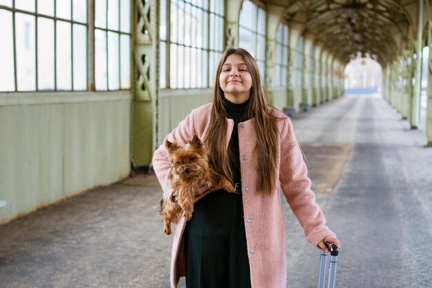 Turista viajante mulher anda com bagagem e cachorro na estação de trem em casaco rosa, o conceito de um ac ...