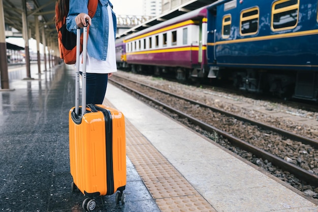 Turista viajero mujer con mochila y maleta naranja en la estación de tren