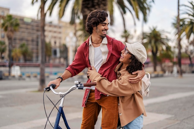 Turistas alegres apaixonados estão se abraçando na rua em pé com uma bicicleta