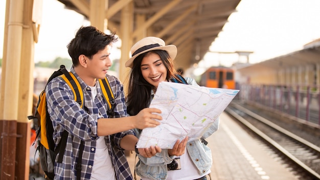 Turistas asiáticos con backpackas usando un mapa en la estación de tren