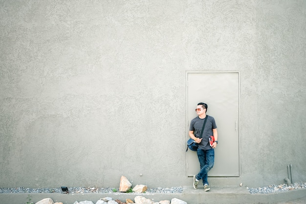 Turistas asiáticos del hombre que se colocan delante de una pared gris.