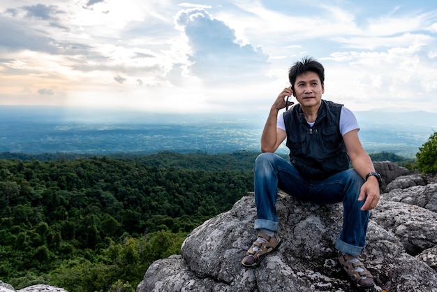 Turistas asiáticos que usan el teléfono móvil Hablan con amigos mientras él estaba en la cima de la montaña