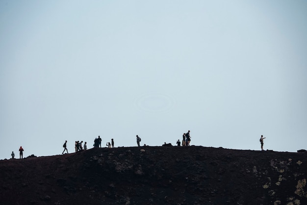 Turistas caminando por el monte etna volcánico con cielo ahumado en el fondo