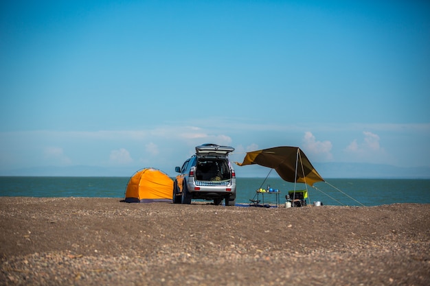 Turistas en coche con una carpa en la orilla del lago.