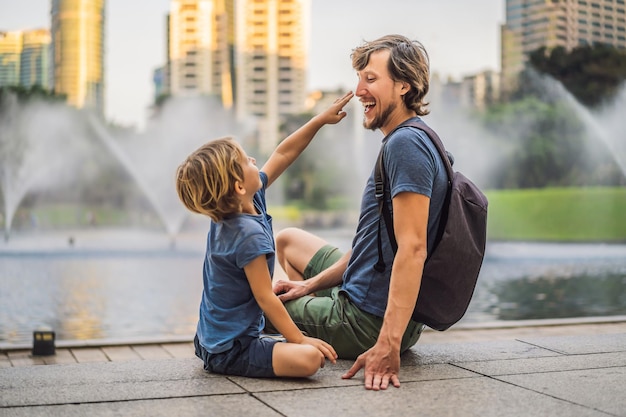 Turistas de pai e filho no fundo da fonte no lago à noite perto de twin towers com cidade ao fundo kuala lumpur malásia