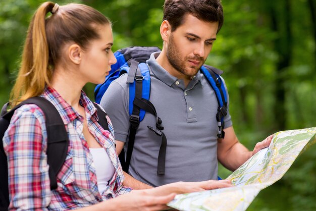 Turistas examinando el mapa. Pareja joven pensativa con mochilas examinando el mapa mientras está de pie en la naturaleza