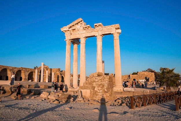 Turistas explorando antigas ruínas do templo de Apolo no litoral ao entardecer