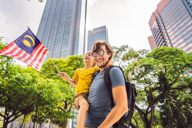 Foto turistas de papá e hijo en malasia con la bandera de malasia cerca de los rascacielos viajando con el concepto de niños