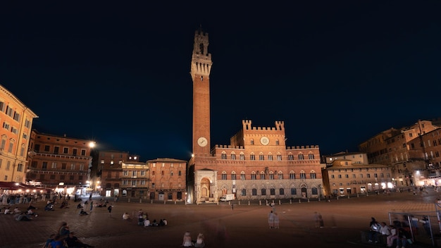 Foto turistas en la piazza del campo con el palazzo pubblico y la torre torre del mangia por la noche siena italia