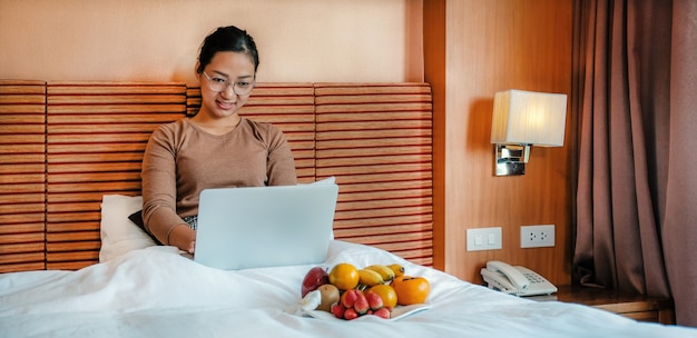 Los turistas usaban una computadora portátil y comían frutas en la cama en el concepto de comida saludable de la habitación del hotel de lujo