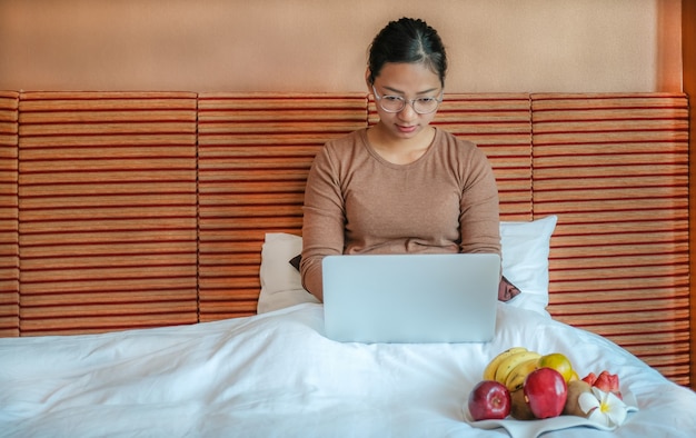 Los turistas usaban una computadora portátil y comían frutas en la cama en el concepto de comida saludable de la habitación del hotel de lujo